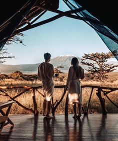 two people standing in front of a tent looking out at the mountains and grass below