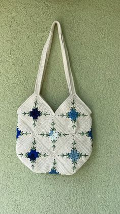 a white bag hanging on the wall with blue and green flowers in it's center