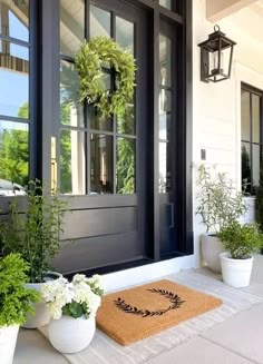 front door with wreath and potted plants next to it on the porch area rug