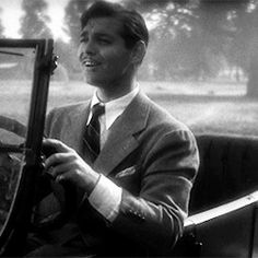 a black and white photo of a man in a suit sitting in an old car