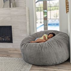 a woman laying on top of a bean bag chair in a living room next to a fireplace