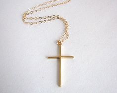 a gold cross necklace on a white surface with a chain hanging from the neckline