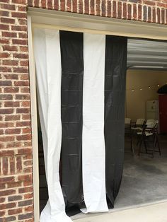 an open garage door with black and white drapes on it's sides, in front of a brick building