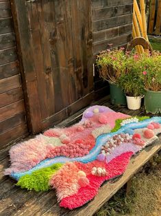 a colorful rug is laying on a wooden bench next to potted plants and flowers