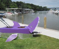 a large purple shark sculpture sitting on top of a lush green field next to a river