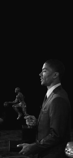 a man in a suit and tie holding a trophy next to a small statue on a table