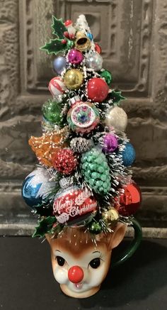 a ceramic christmas tree with ornaments on it's head and nose in front of a wall