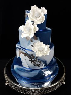 a three tiered blue and white cake with flowers on the top is sitting on a plate