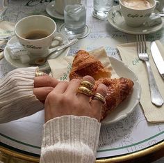 a person's hand holding onto a pastry on a table with coffee and silverware