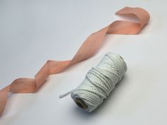 a spool of pink ribbon next to a roll of twine on a white surface