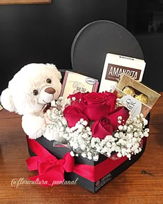 a white teddy bear sitting in a box with flowers and chocolates on the table