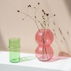 two vases with flowers in them sitting on a table next to a cup and container