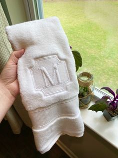 a hand holding a white towel with the letter m on it in front of a window