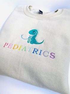 Get cozy in style with the "Pediatrics" Sweatshirt! This comfy long-sleeved sweater features Neutral toned colors showcasing the Pediatric Dinosaur design, making it the perfect gift for your friends, family, or yourself! So whether you're cozying up at home or pulling an overnight shift, this sweatshirt has got your back. -Embroidered on a cotton/polyester blend crewneck sweatshirt, this design is simple and minimalistic, perfect for every outfit! -Embroidery design measures 5" x 7". -See product pictures for shirt sizing chart. -All sweatshirts are handmade on an embroidery machine so there may be slight differences, but we only sell the sweatshirts that meet our high-quality standards. -To maintain the quality of your sweatshirt and the embroidery design make sure to wash with care. We Pediatric Nurse Outfits, Dinosaur Sweatshirt, Nursing Sweatshirt, Nursing Graduation Pictures, Or Nurse, Nursing Accessories