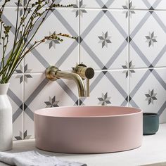 a pink bowl sink sitting on top of a counter next to a vase with flowers