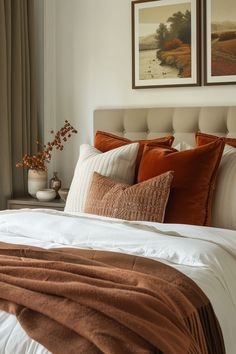 a bed with orange and white pillows in a bedroom next to two pictures on the wall