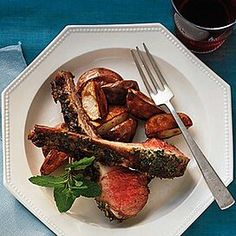 a white plate topped with meat and potatoes next to a glass of wine on top of a blue table cloth