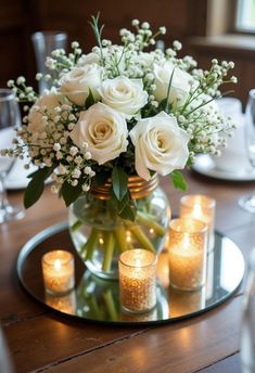 white roses and baby's breath in a glass vase on a table with candles