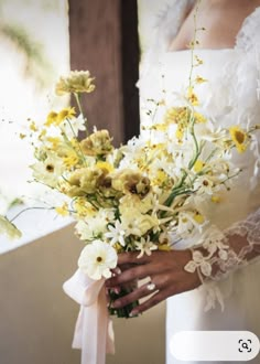 a bride holding a bouquet of yellow and white flowers