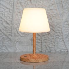 a wooden table lamp with a white shade on it's base, against a textured wall