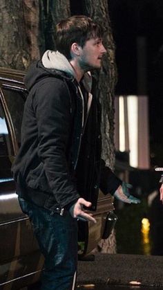 a man standing next to a parked car talking to another man with his hand on the door handle