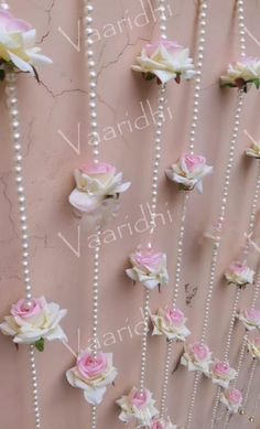 pink and white flowers are hanging on the wall with pearls attached to each bead