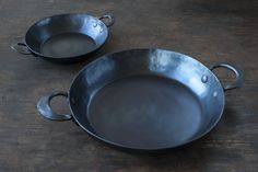 two metal pans sitting on top of a wooden table next to eachother