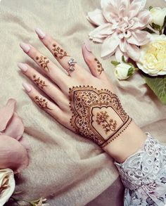 a woman's hand with henna tattoos on it and flowers in the background