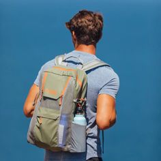 a man with a backpack and water bottle in his hand looking at the blue sky