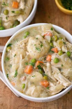 two bowls filled with chicken and dumplings on top of a wooden table next to carrots