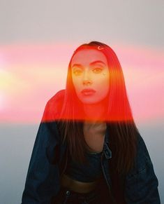 a woman with long red hair sitting in front of a pink and orange light that is shining on her face