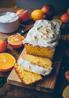 slices of cake with icing and oranges around it on a wooden cutting board