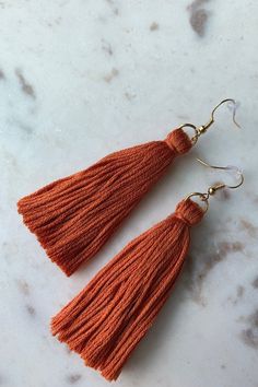 two orange tassels hanging from gold hooks on a white marble countertop,