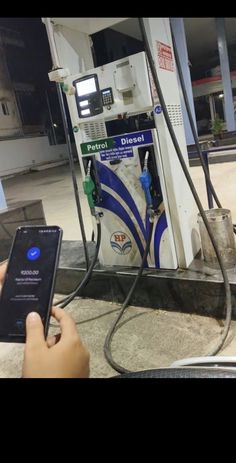 a person holding a cell phone in front of a gas station with an electronic device