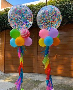 two balloons with streamers and confetti on them are standing in front of a fence