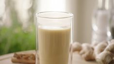 a glass filled with liquid sitting on top of a table next to some ginger stalks