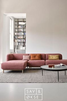 a living room with a pink couch, coffee table and bookshelf in the background