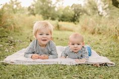 two toddlers laying on a blanket in the grass