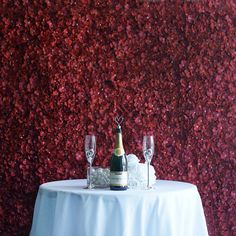 a table with two wine glasses and a bottle on it next to a red wall