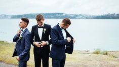 three young men in tuxedos standing by the water