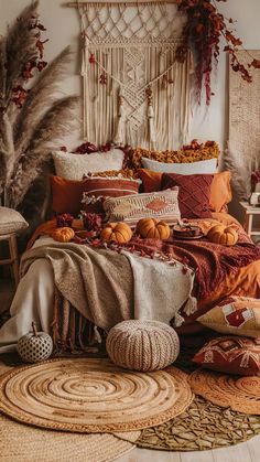 a bed covered in lots of pillows and blankets next to a rug with pumpkins on it