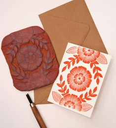 an orange and white flowered card next to a brown envelope with a rubber stamp