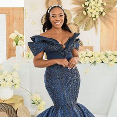 a woman in a blue dress standing next to a white table with flowers on it