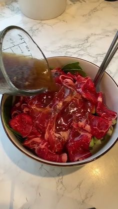 a bowl filled with meat and vegetables on top of a white countertop next to a measuring cup