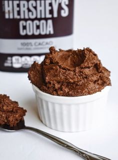 there is a spoon that is next to a bowl of chocolate ice cream and a can of hershey's cocoa