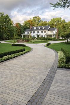 a large white house sitting on top of a lush green field next to a driveway