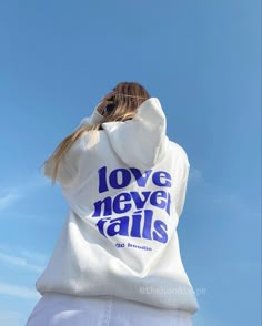 a woman wearing a white hoodie with the words love never falls printed on it