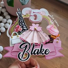 someone holding up a pink and white cake topper with the number five on it