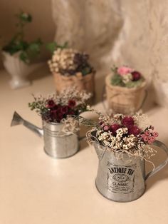 three metal watering cans with flowers in them