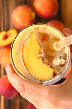 a person is holding a glass with some fruit in it and there are peaches on the table